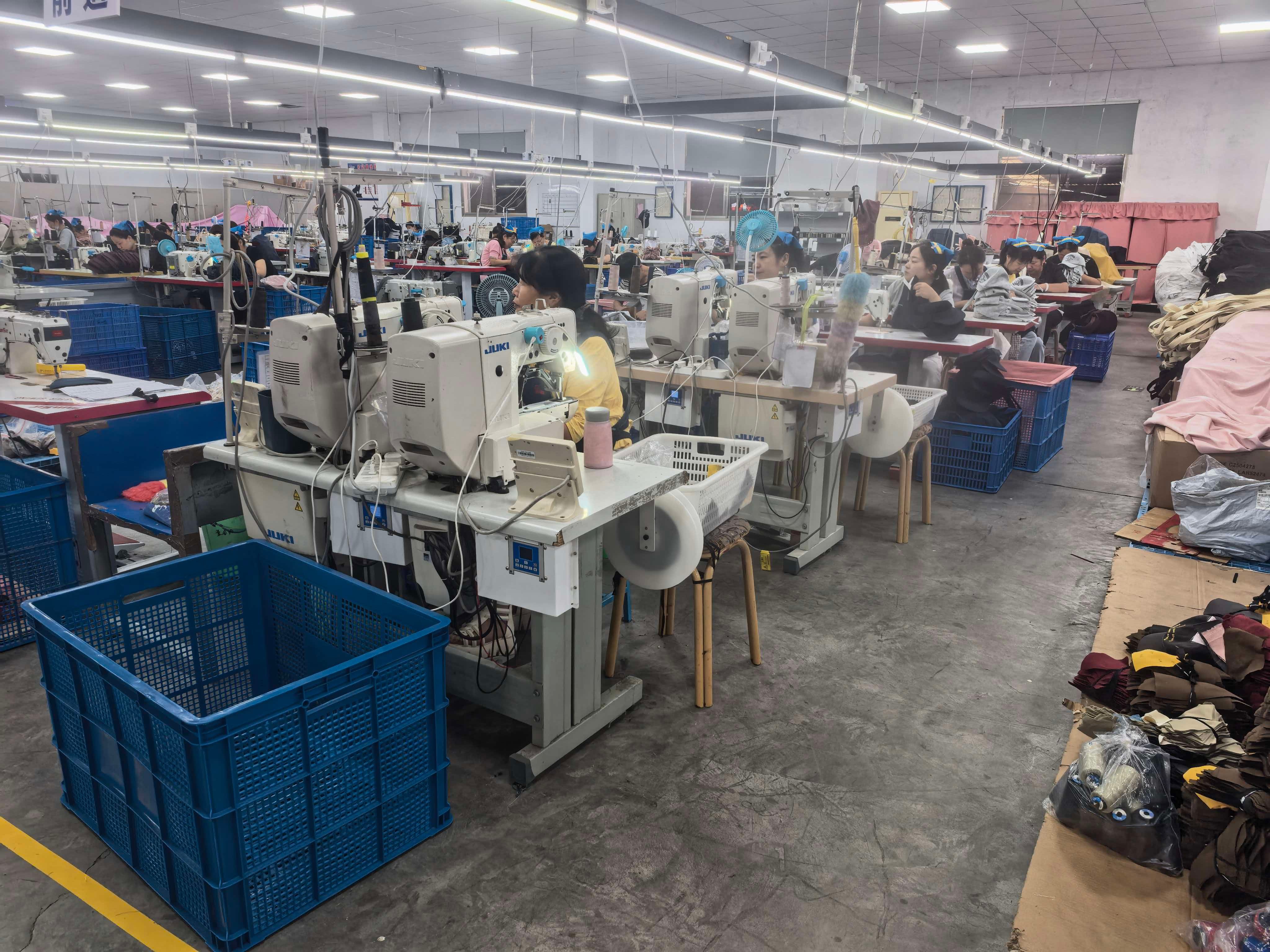 Workers at rows of sewing stations on the factory floor, with blue crates between the tables