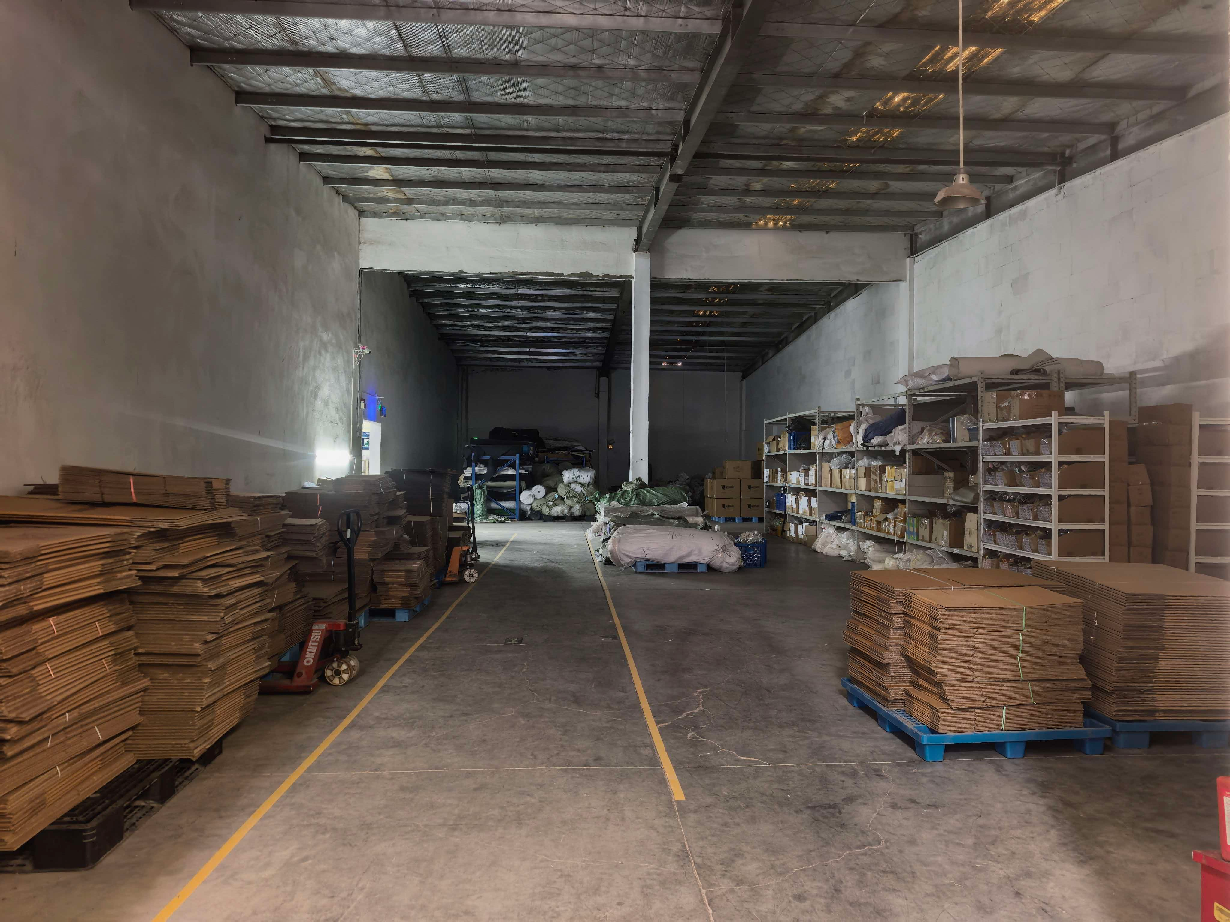 Warehouse aisle with stacked flat cartons and shelving with boxed components